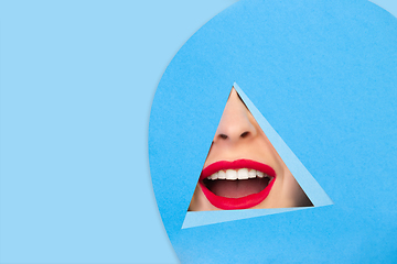 Image showing Female red lips peeking throught triangle in blue background