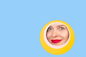 Image showing Female face with red lips peeking throught circle in blue background