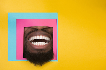 Image showing Mouth of african-american man peeking throught square in yellow background