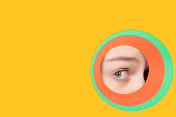 Image showing Female eye peeking throught circle in yellow background