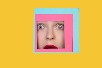 Image showing Face of caucasian woman peeking throught square in yellow background