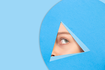 Image showing Female eye looking, peeking throught triangle in blue background