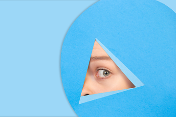 Image showing Female eye looking, peeking throught triangle in blue background