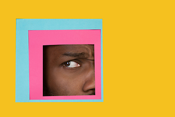 Image showing Eye of african-american man peeking throught square in yellow background