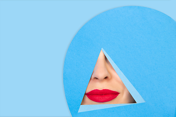 Image showing Female red lips peeking throught triangle in blue background