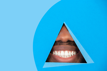 Image showing Lips of african-american man peeking throught triangle in blue background