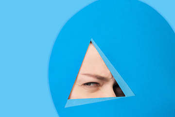 Image showing Face of caucasian woman peeking throught triangle in blue background