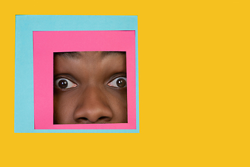 Image showing Face of african-american man peeking throught square in yellow background