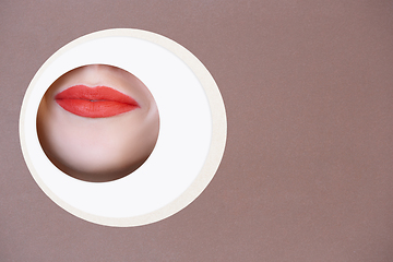 Image showing Female face with red lips peeking throught circle in brown background