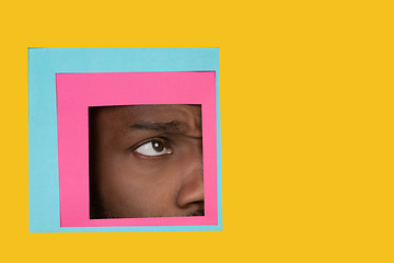 Image showing Eye of african-american man peeking throught square in yellow background