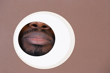 Image showing Lips of african-american man peeking throught circle in brown background