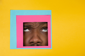 Image showing Face of african-american man peeking throught square in yellow background