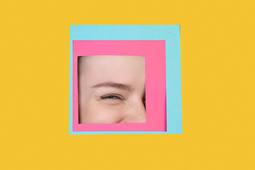 Image showing Face of caucasian woman peeking throught square in yellow background