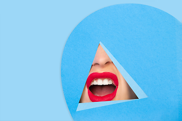 Image showing Female red lips peeking throught triangle in blue background