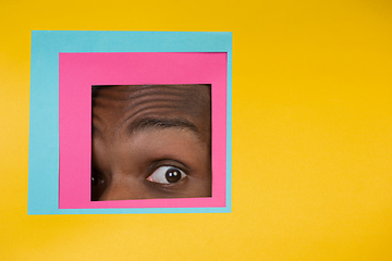 Image showing Eye of african-american man peeking throught square in yellow background