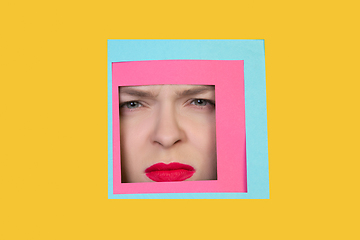 Image showing Face of caucasian woman peeking throught square in yellow background