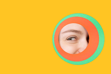 Image showing Female eye peeking throught circle in yellow background