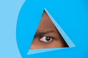 Image showing Eye of african-american man peeking throught triangle in blue background