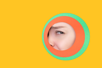 Image showing Female eye peeking throught circle in yellow background