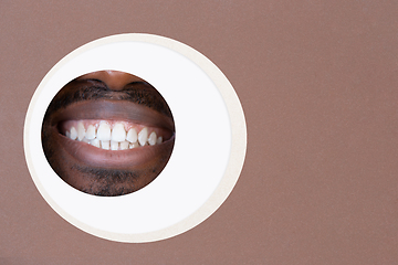 Image showing Lips of african-american man peeking throught circle in brown background