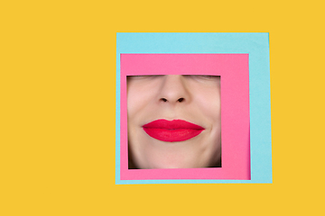 Image showing Face of caucasian woman peeking throught square in yellow background