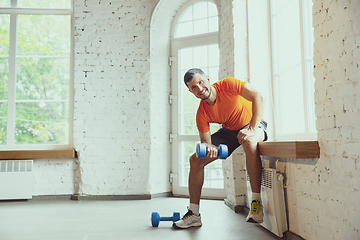 Image showing Young caucasian man training at home during quarantine of coronavirus outbreak, doing exercises of fitness, aerobic. Staying sportive during insulation.