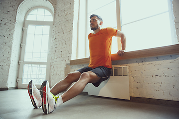 Image showing Young caucasian man training at home during quarantine of coronavirus outbreak, doing exercises of fitness, aerobic. Staying sportive during insulation.