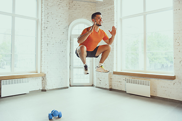 Image showing Young caucasian man training at home during quarantine of coronavirus outbreak, doing exercises of fitness, aerobic. Staying sportive during insulation.