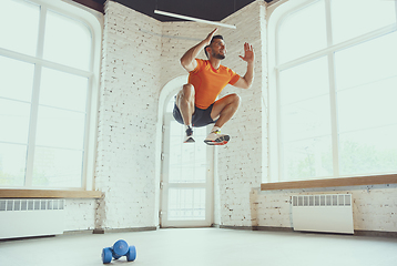 Image showing Young caucasian man training at home during quarantine of coronavirus outbreak, doing exercises of fitness, aerobic. Staying sportive during insulation.