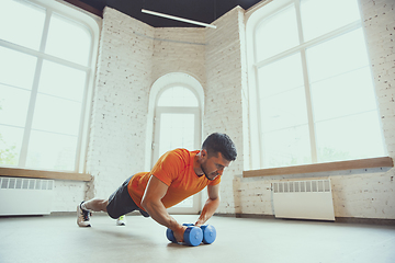 Image showing Young caucasian man training at home during quarantine of coronavirus outbreak, doing exercises of fitness, aerobic. Staying sportive during insulation.