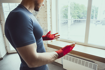 Image showing Young caucasian man training at home during quarantine of coronavirus outbreak, doing exercises of fitness, aerobic. Staying sportive during insulation.