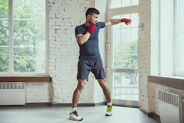 Image showing Young caucasian man training at home during quarantine of coronavirus outbreak, doing exercises of fitness, aerobic. Staying sportive during insulation.