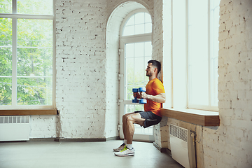 Image showing Young caucasian man training at home during quarantine of coronavirus outbreak, doing exercises of fitness, aerobic. Staying sportive during insulation.