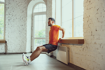 Image showing Young caucasian man training at home during quarantine of coronavirus outbreak, doing exercises of fitness, aerobic. Staying sportive during insulation.