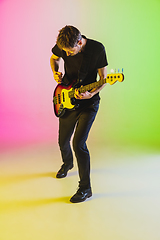 Image showing Young caucasian musician playing bass guitar in neon light on pink-green background