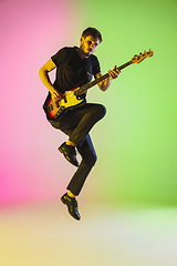 Image showing Young caucasian musician playing bass guitar in neon light on pink-green background