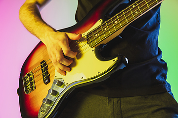 Image showing Close up musician hands playing bass guitar on gradient studio background in neon light