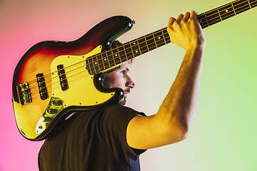 Image showing Young caucasian musician playing bass guitar in neon light on pink-green background