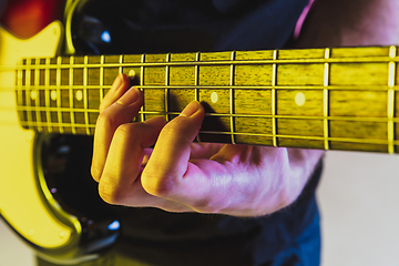 Image showing Close up musician hands playing bass guitar on gradient studio background in neon light