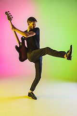 Image showing Young caucasian musician playing bass guitar in neon light on pink-green background