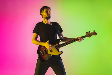 Image showing Young caucasian musician playing bass guitar in neon light on pink-green background