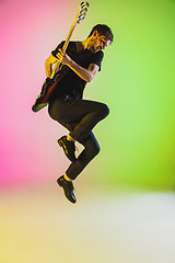 Image showing Young caucasian musician playing bass guitar in neon light on pink-green background