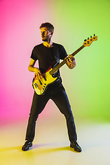 Image showing Young caucasian musician playing bass guitar in neon light on pink-green background