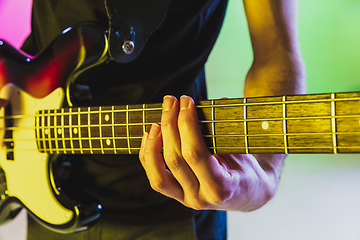 Image showing Close up musician hands playing bass guitar on gradient studio background in neon light