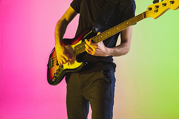 Image showing Young caucasian musician playing bass guitar in neon light on pink-green background