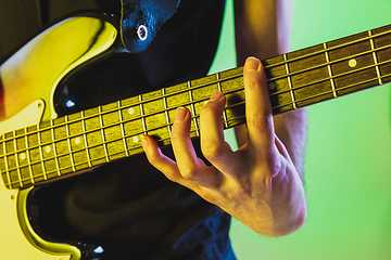 Image showing Close up musician hands playing bass guitar on gradient studio background in neon light