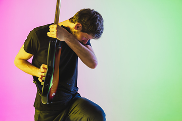 Image showing Young caucasian musician playing bass guitar in neon light on pink-green background