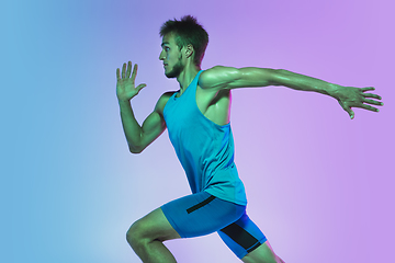 Image showing Full length portrait of active young caucasian running, jogging man on gradient studio background in neon light