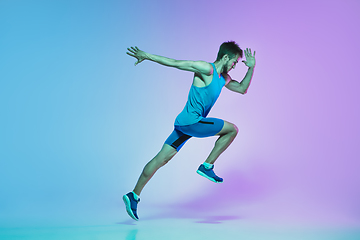 Image showing Full length portrait of active young caucasian running, jogging man on gradient studio background in neon light