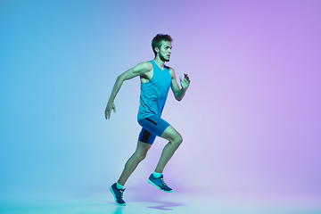 Image showing Full length portrait of active young caucasian running, jogging man on gradient studio background in neon light